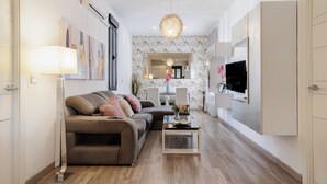Un salon moderne avec un canapé, une table basse, un téléviseur fixé au mur et un luminaire suspendu.