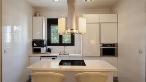 Une cuisine moderne dotée d’un îlot central, d’appareils électroménagers intégrés et de luminaires suspendus.