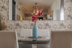 Un coin repas comprenant une table, des chaises, un vase avec des fleurs et un mur décoré de motifs.