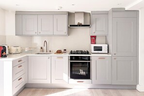 A modern kitchen with grey cabinets, a built-in oven, a microwave, and a gas stove.