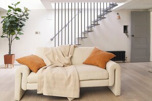 A living room with a sofa, a potted plant, and a staircase.