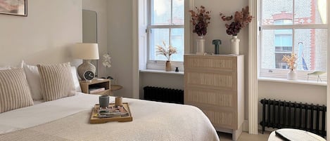 A bedroom with a bed, bedside table, lamp, dresser, and window with a view of buildings.