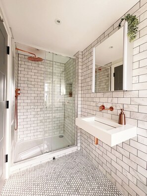 Ein modernes Badezimmer mit einer einteiligen Duschkabine, einem weißen Waschbecken mit Kupferarmaturen und einem Spiegel darüber.