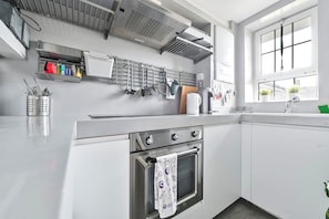 A modern kitchen with stainless steel appliances, a hanging utensil rack, and a window with potted plants. - Canary Wharf Skyline Views (Greater London)