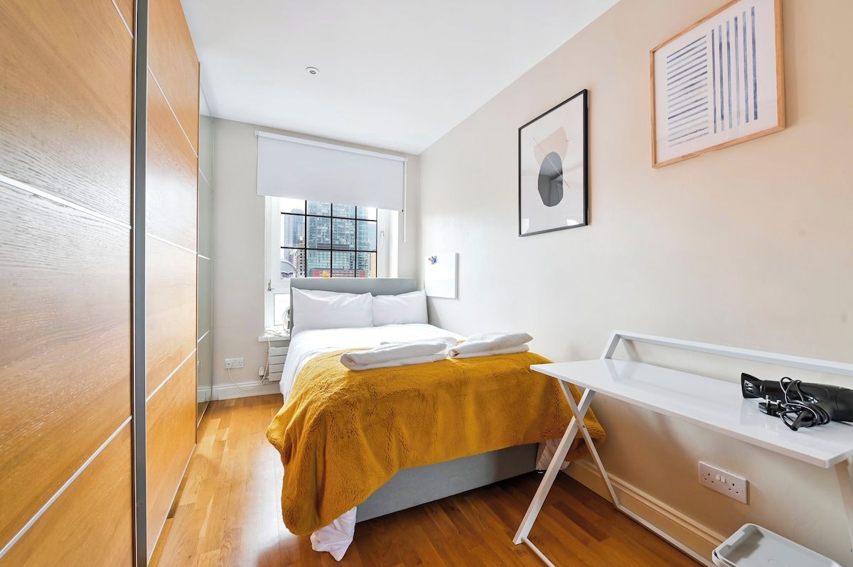 A modern hotel room with a bed, a white desk, and a window with a city view.