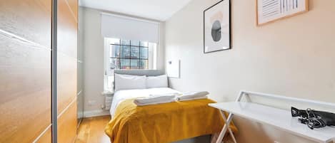 A modern hotel room with a bed, a white desk, and a window with a city view.