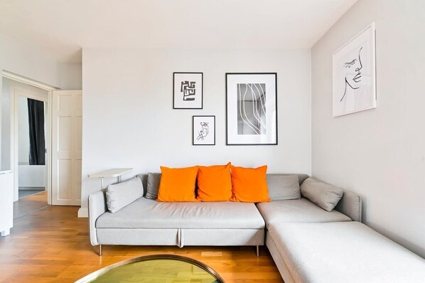 Un salon moderne avec un canapé d’angle gris, trois œuvres d’art encadrées accrochées au mur et un plancher en bois.
