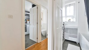 Pasillo que conduce a un baño con inodoro, lavamanos y ventana.