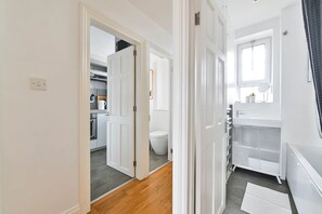 A hallway leading to a bathroom with a toilet, sink, and window.