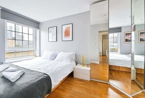 Une chambre moderne avec un grand lit, une table de chevet, un miroir et une fenêtre donnant sur la ville.