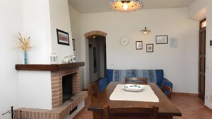 A dining area with a brick fireplace, a long wooden table, blue upholstered chairs, and a decorative ceiling light fixture. - Apartment 'Azzurro La Valle Del Sole' with Mountain View and Wi-Fi (Castiglione dʼOrcia)