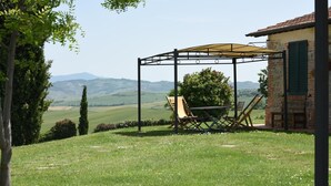 A patio with a table and chairs, a pergola, and a view of rolling hills. - Apartment 'Azzurro La Valle Del Sole' with Mountain View and Wi-Fi (Castiglione dʼOrcia)