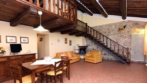 Un amplio salón con una escalera de madera, una mesa de comedor con sillas, un sofá y una chimenea.