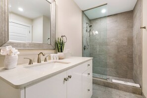 Une salle de bain moderne avec un grand miroir, un lavabo et un espace douche.