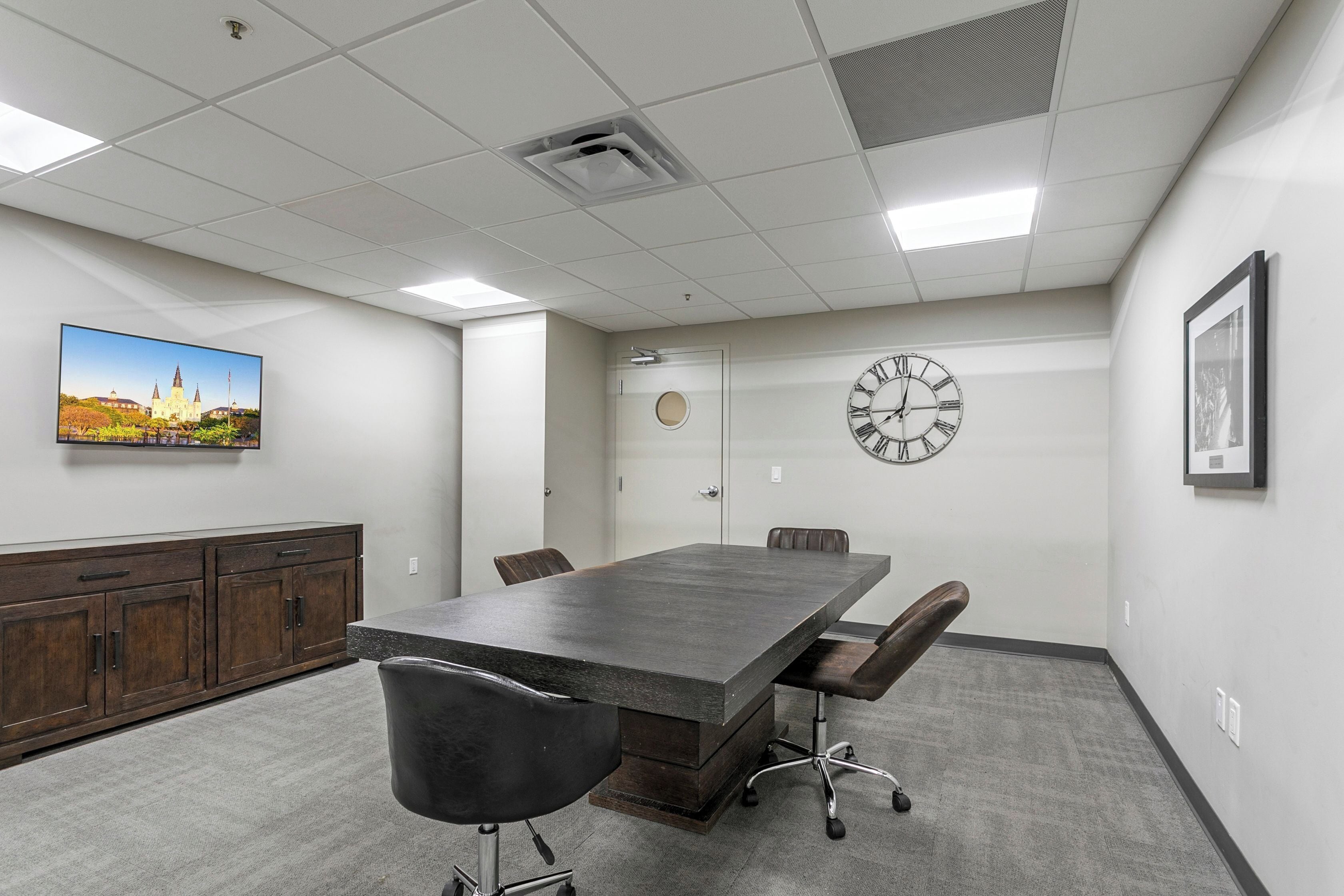 Une salle de conférence avec une grande table, des chaises, une horloge et un tableau encadré au mur.