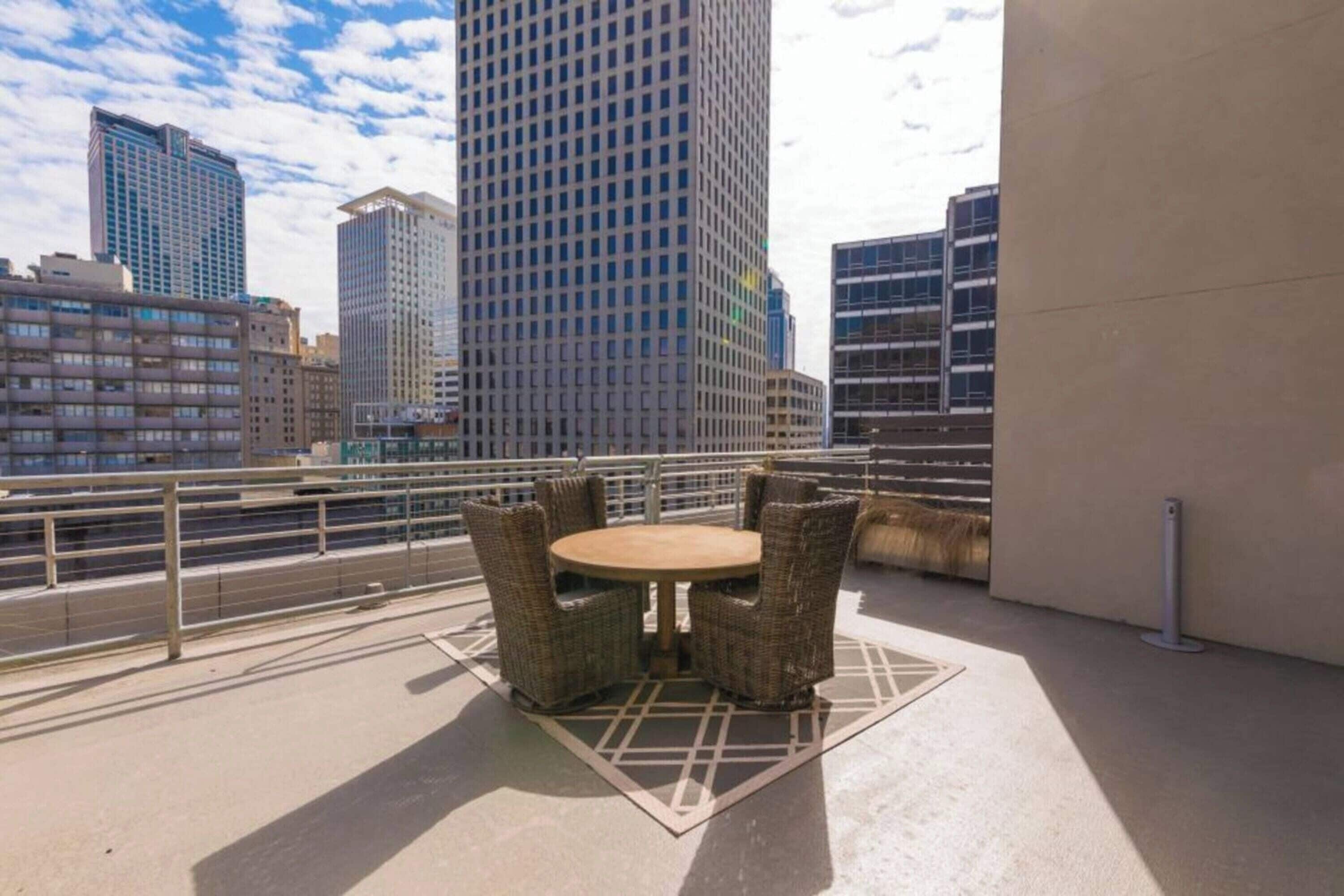 Una terraza en la azotea con mobiliario de mimbre, vistas de edificios de la ciudad y una barandilla metálica.