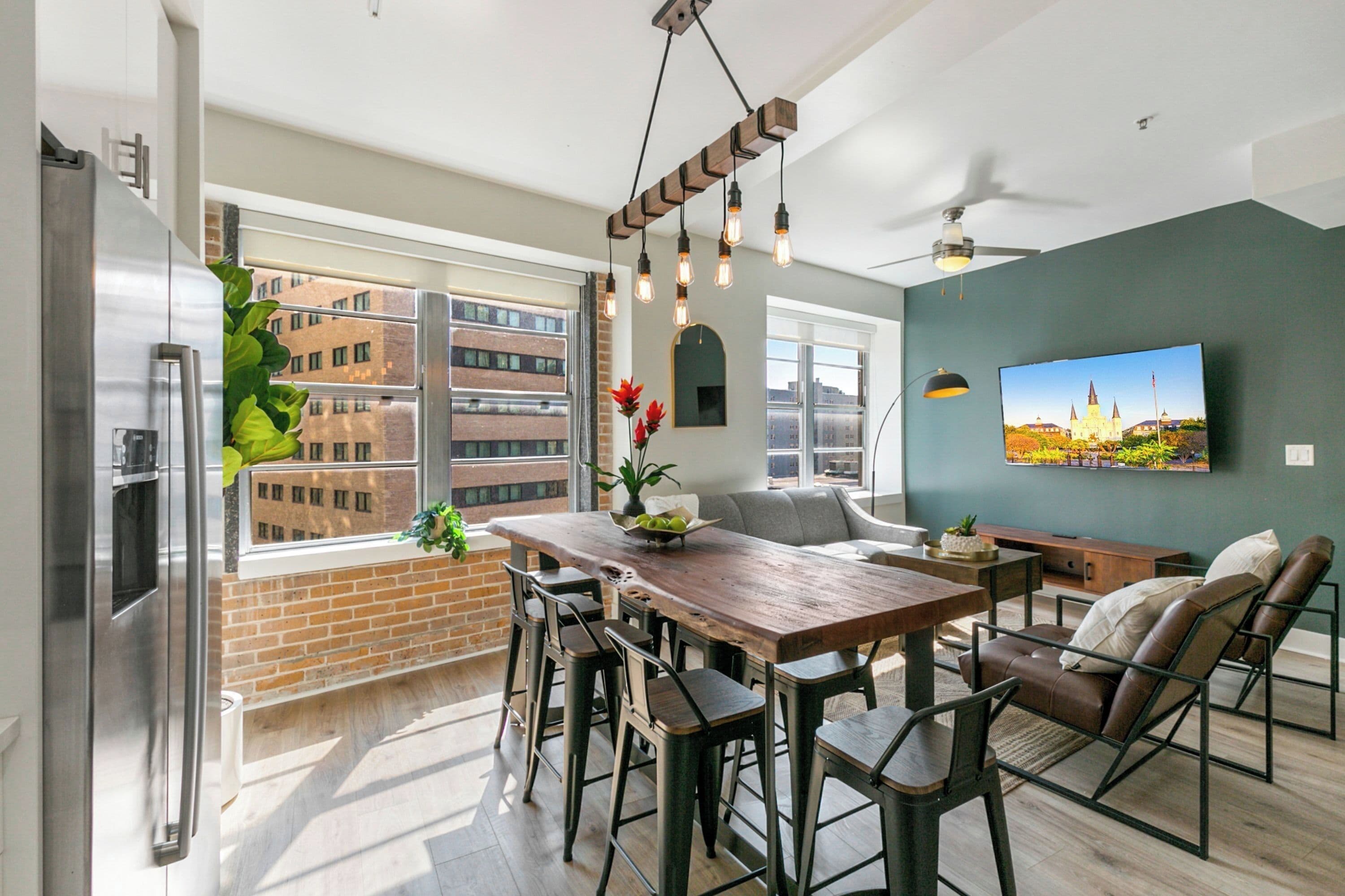 A modern kitchen with a large window, a wooden dining table, bar stools, and a built-in refrigerator.