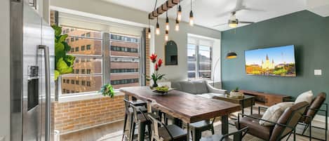A modern kitchen with a large window, a wooden dining table, bar stools, and a built-in refrigerator.