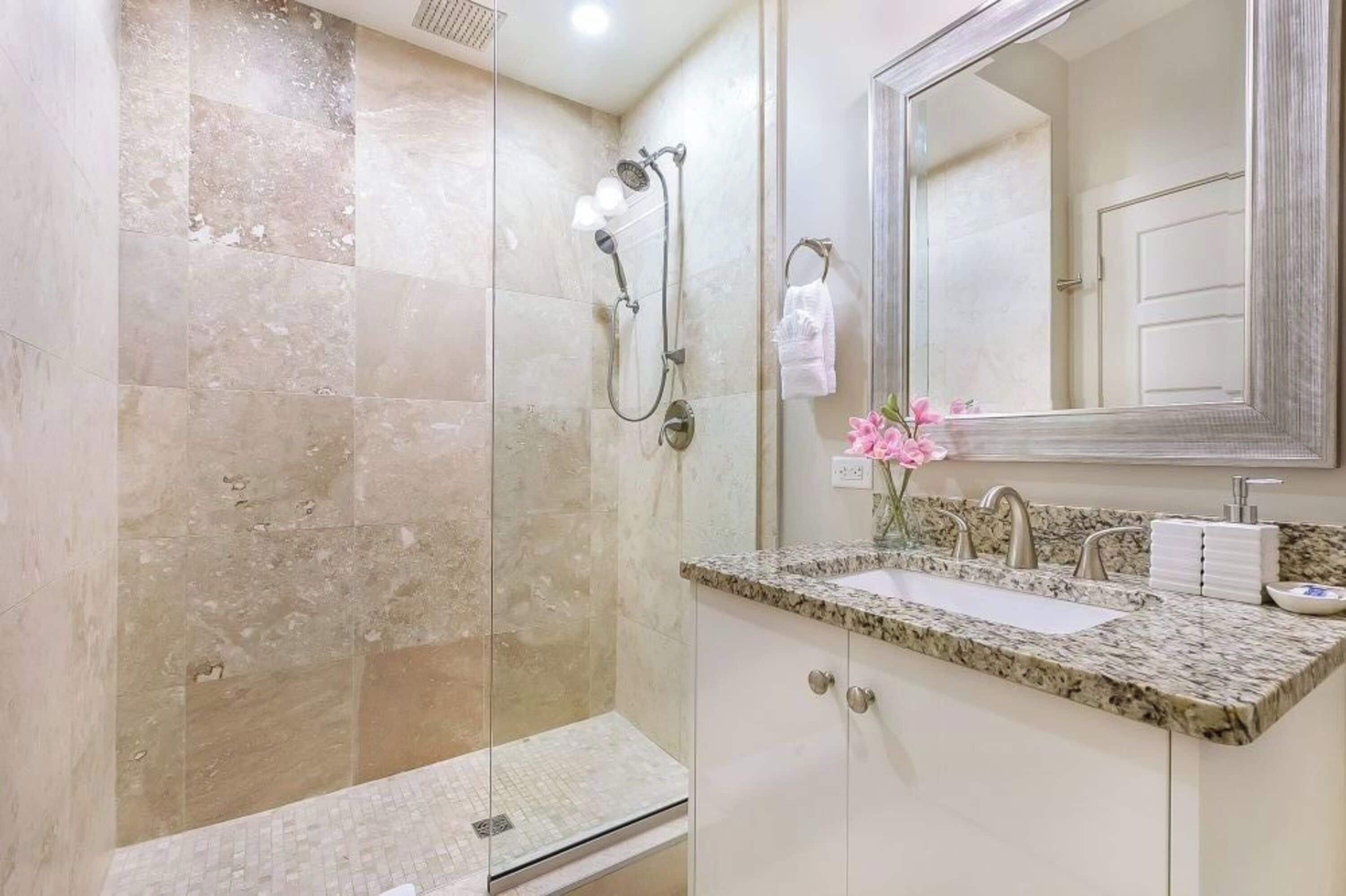 A modern bathroom with a glass-enclosed shower, a granite countertop sink, and a large mirror.