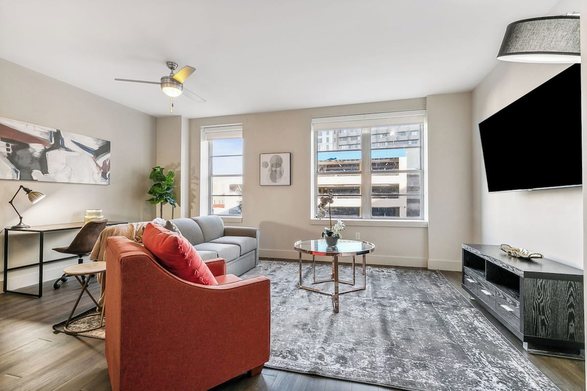A modern living room with a gray sofa, a red armchair, a coffee table, and a TV on a black stand.