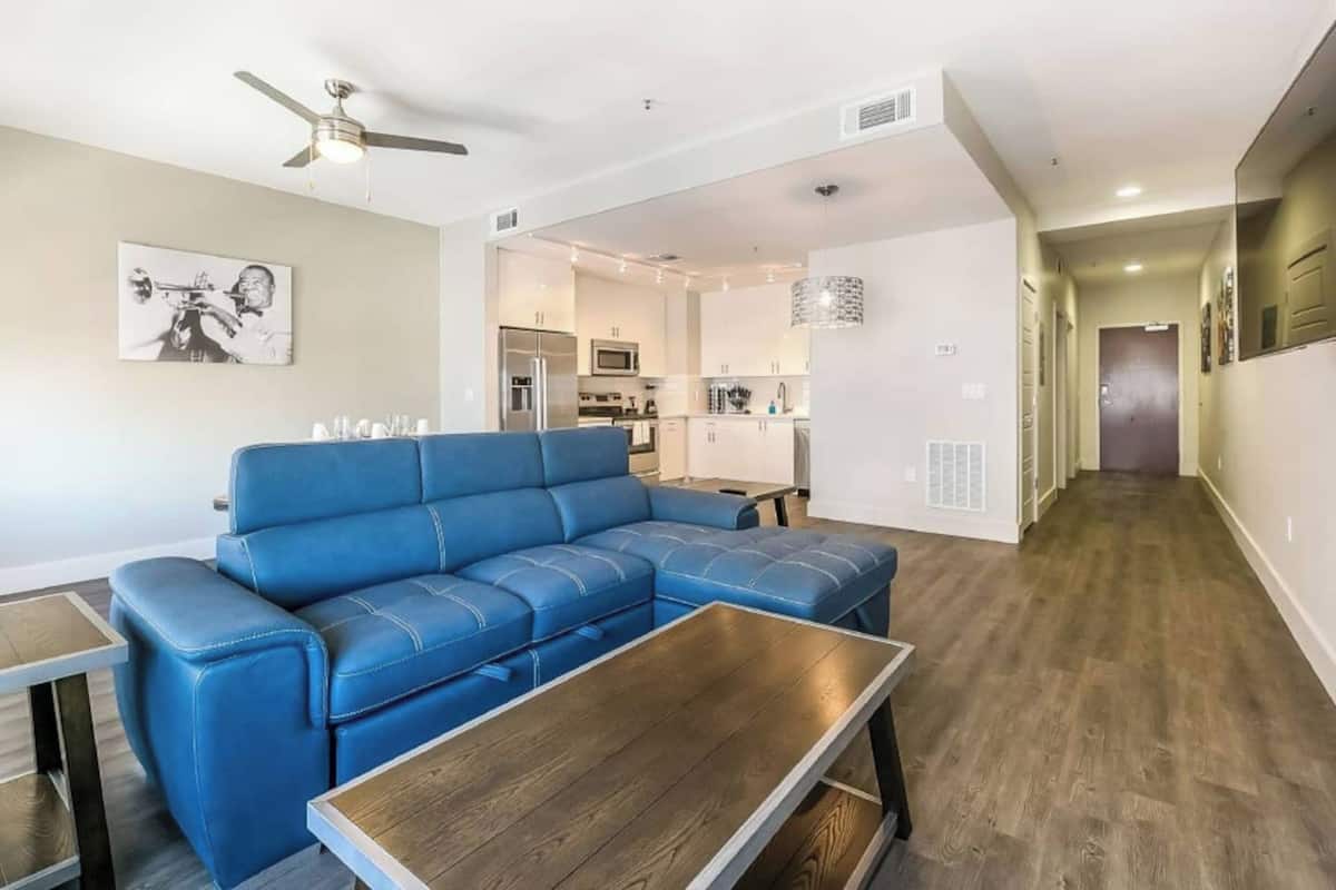 A modern living room with a blue sectional sofa, a wooden coffee table, and a ceiling fan.