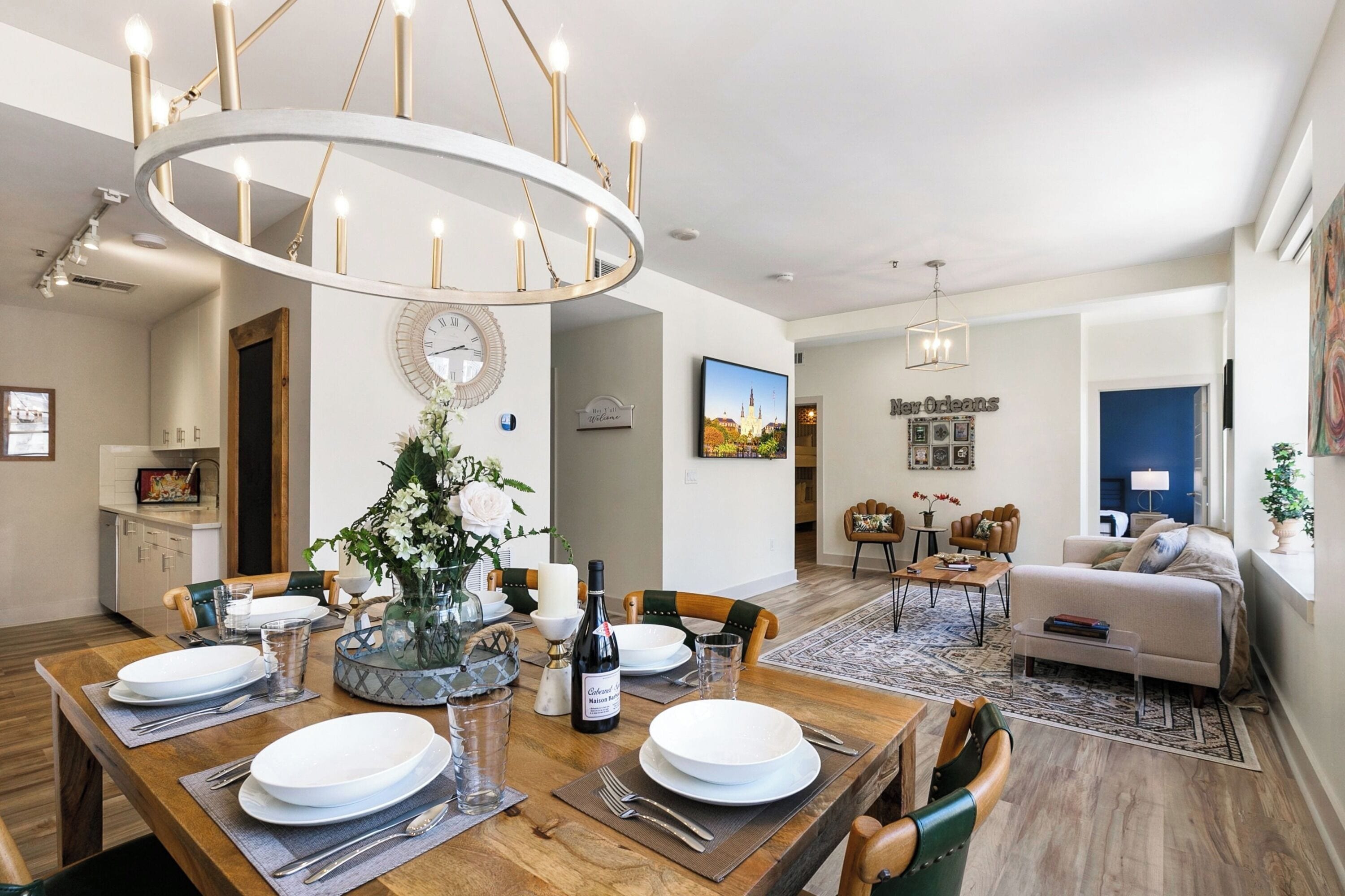 A modern dining area with a wooden table set for four, a chandelier, and a clock on the wall.