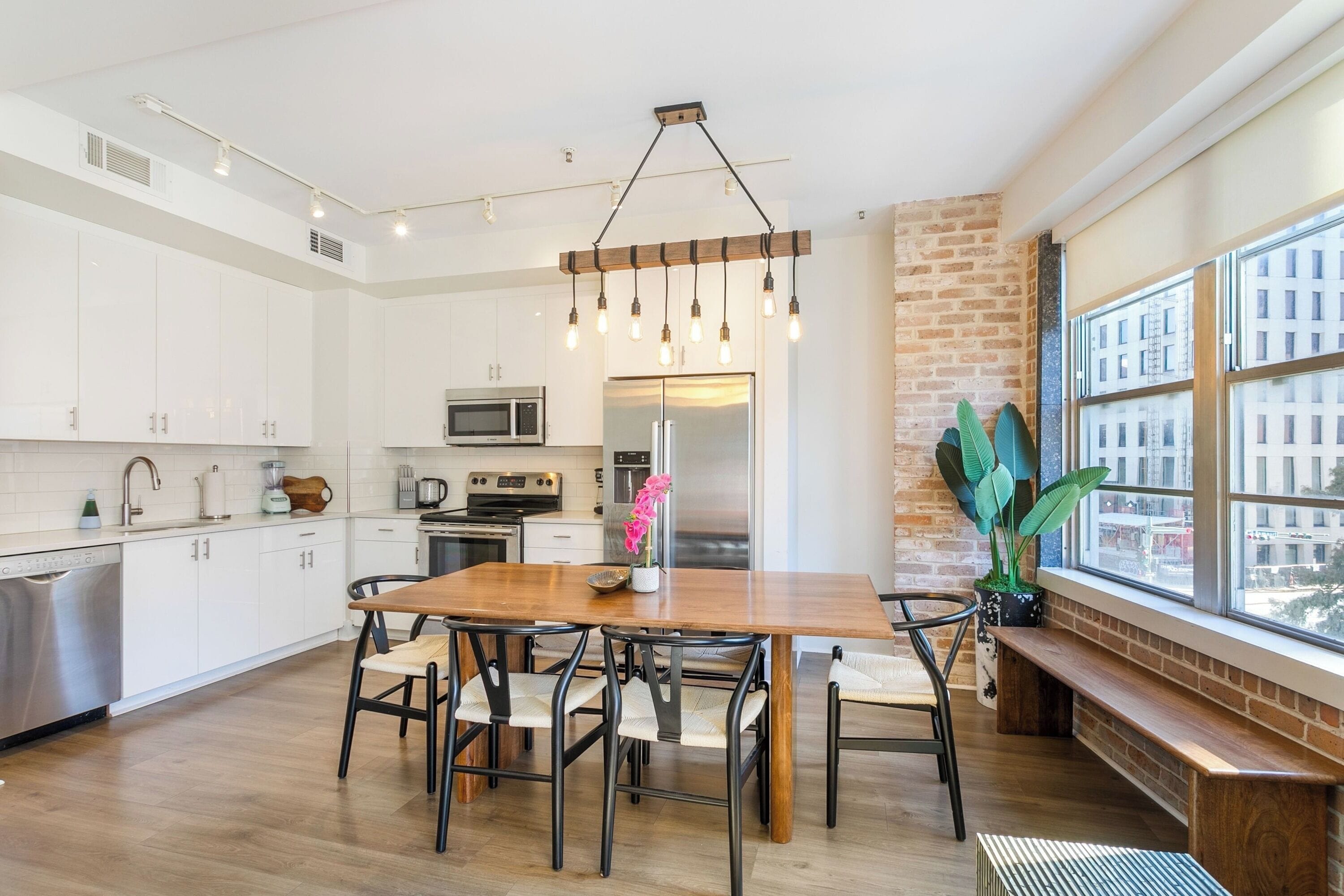 A modern kitchen with white cabinets, a wooden dining table, and a hanging light fixture.
