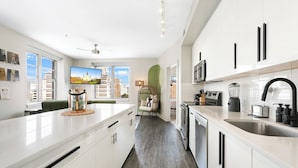 A modern kitchen with white cabinetry, a large island, and a view of the cityscape through the windows. - California Building (New Orleans)