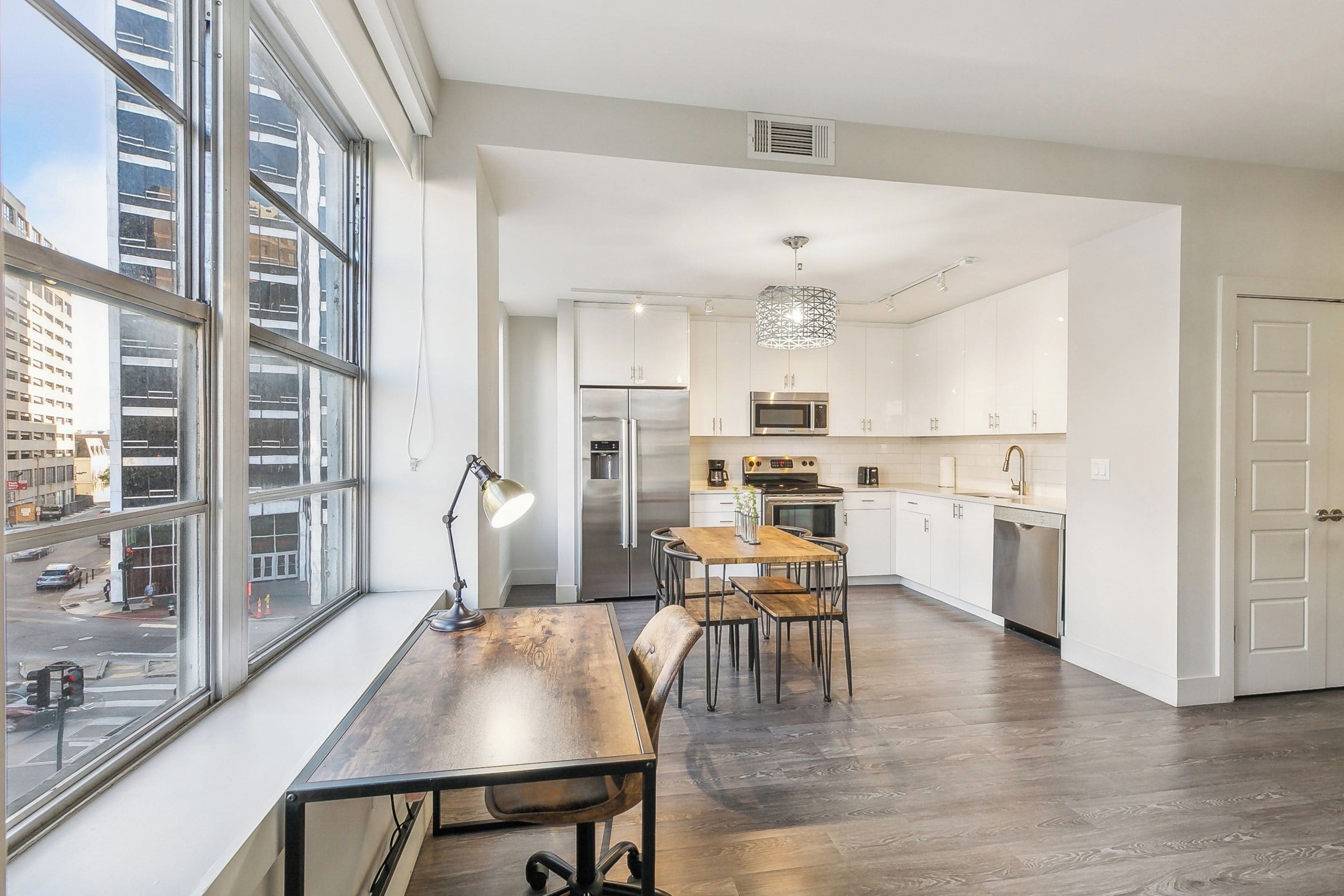Een moderne keuken met witte kasten, roestvrijstalen apparatuur en een eethoek met een houten tafel en stoelen.