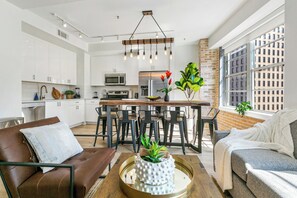 A modern kitchen with white cabinets, a central island, and a hanging light fixture. - California Building (New Orleans)