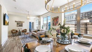A dining area with a wooden table set for four, a chandelier, and a view of the city through large windows. - California Building (New Orleans)