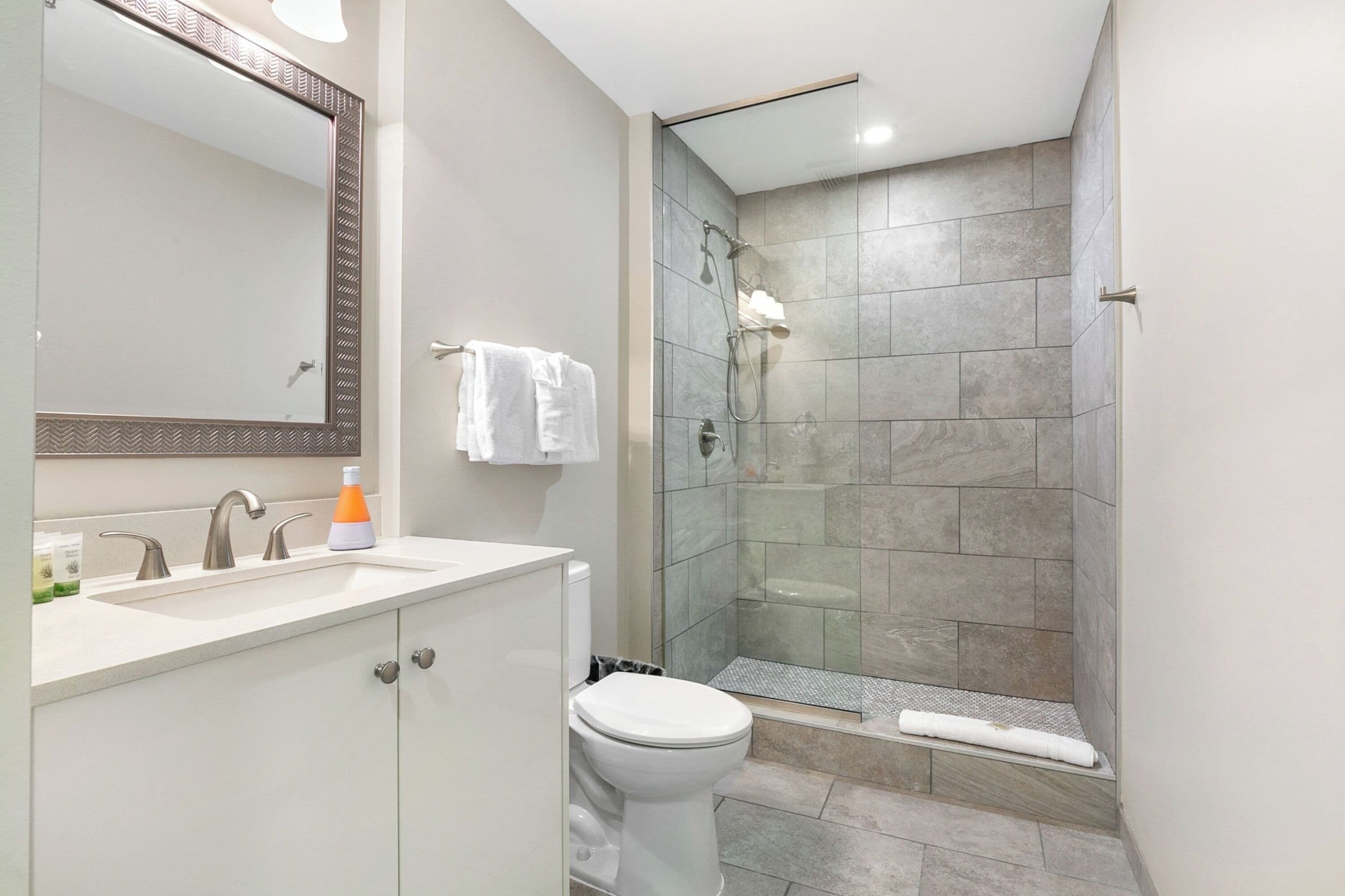 A modern bathroom with a large mirror, a sink with two faucets, a toilet, and a glass-enclosed shower area.