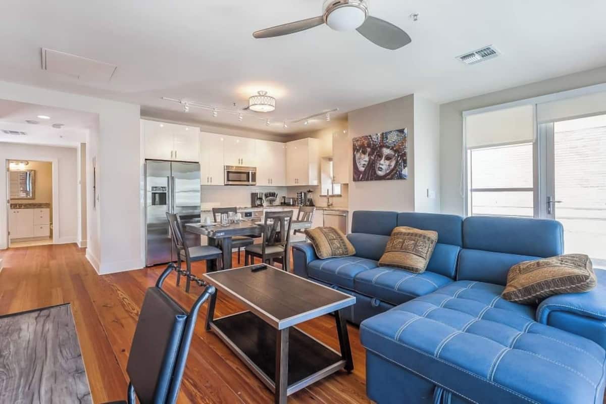 A modern living room with a blue sofa, a coffee table, and a dining area with a kitchen in the background.