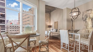 A dining area with a round glass table, wooden chairs, and a view of the city through large windows. - California Building (New Orleans)