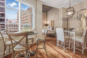 A dining area with a round glass table, wooden chairs, and a view of the city through large windows.