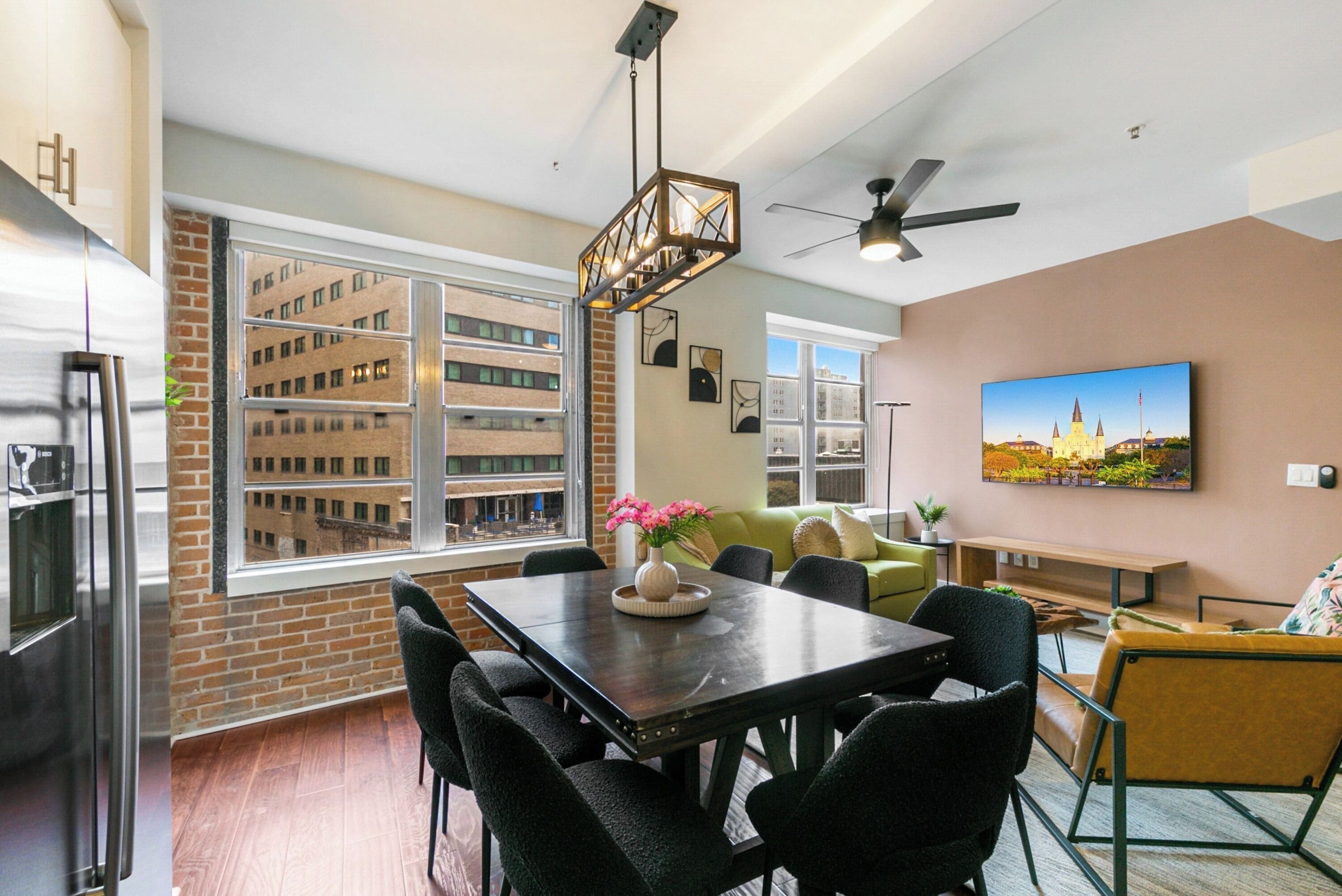 A modern kitchen with a large window, a dining area with a table and chairs, and a ceiling fan.