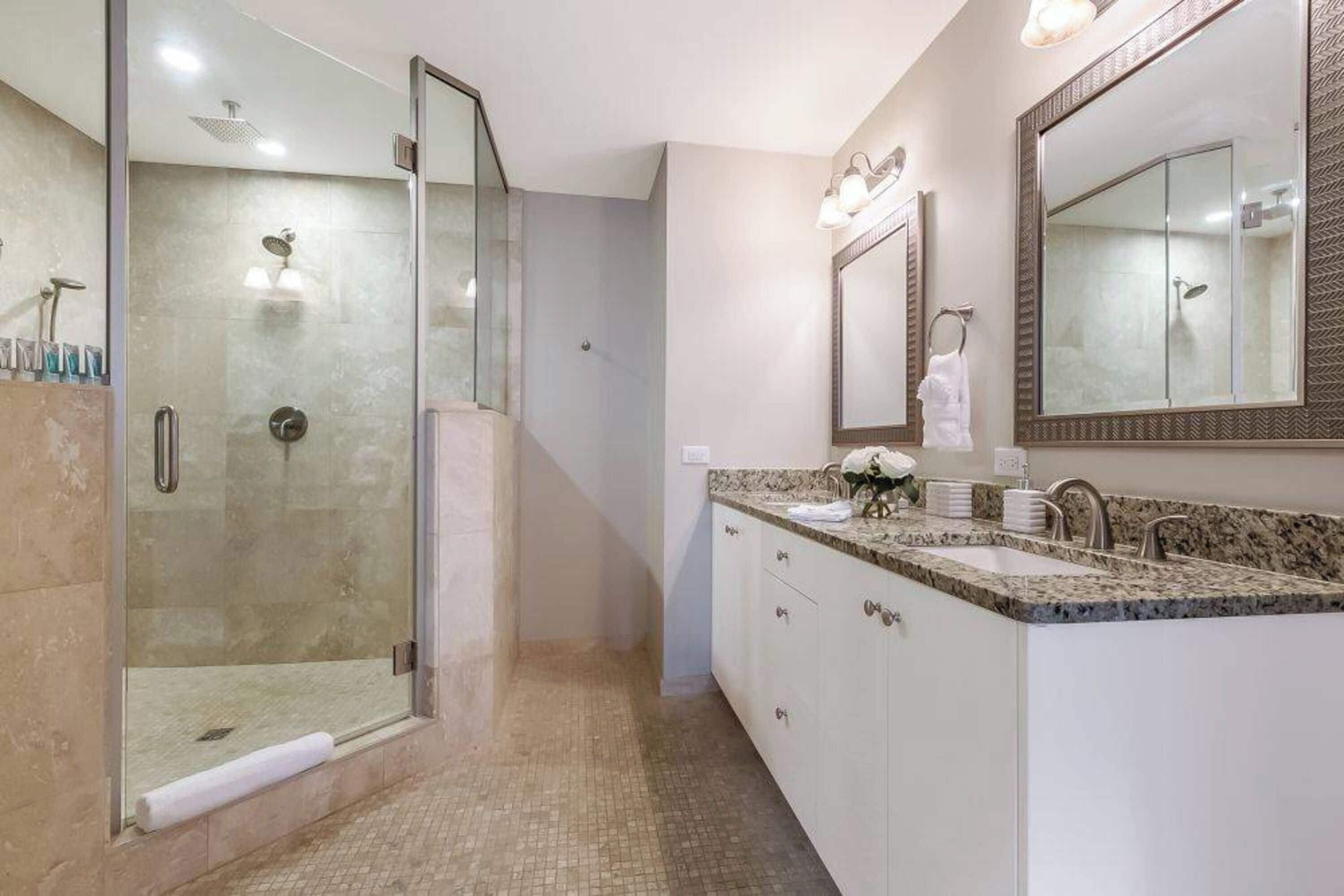 A modern bathroom with a glass-enclosed shower, a vanity with a sink and mirror, and a tiled floor.