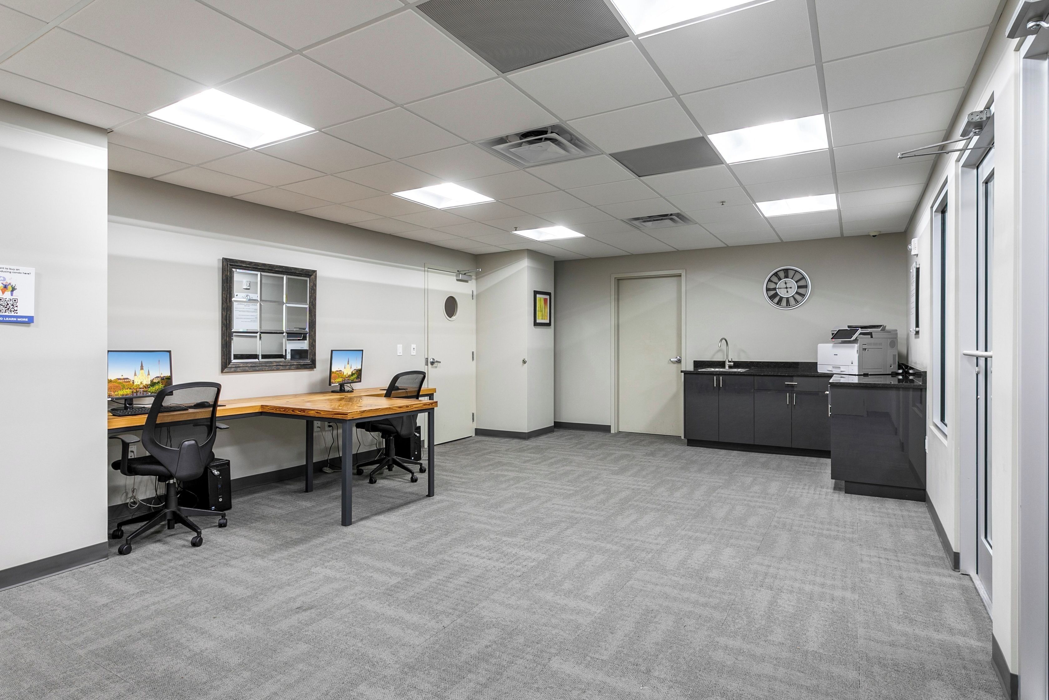 A conference room with a long table, two chairs, a clock, and a kitchenette area.