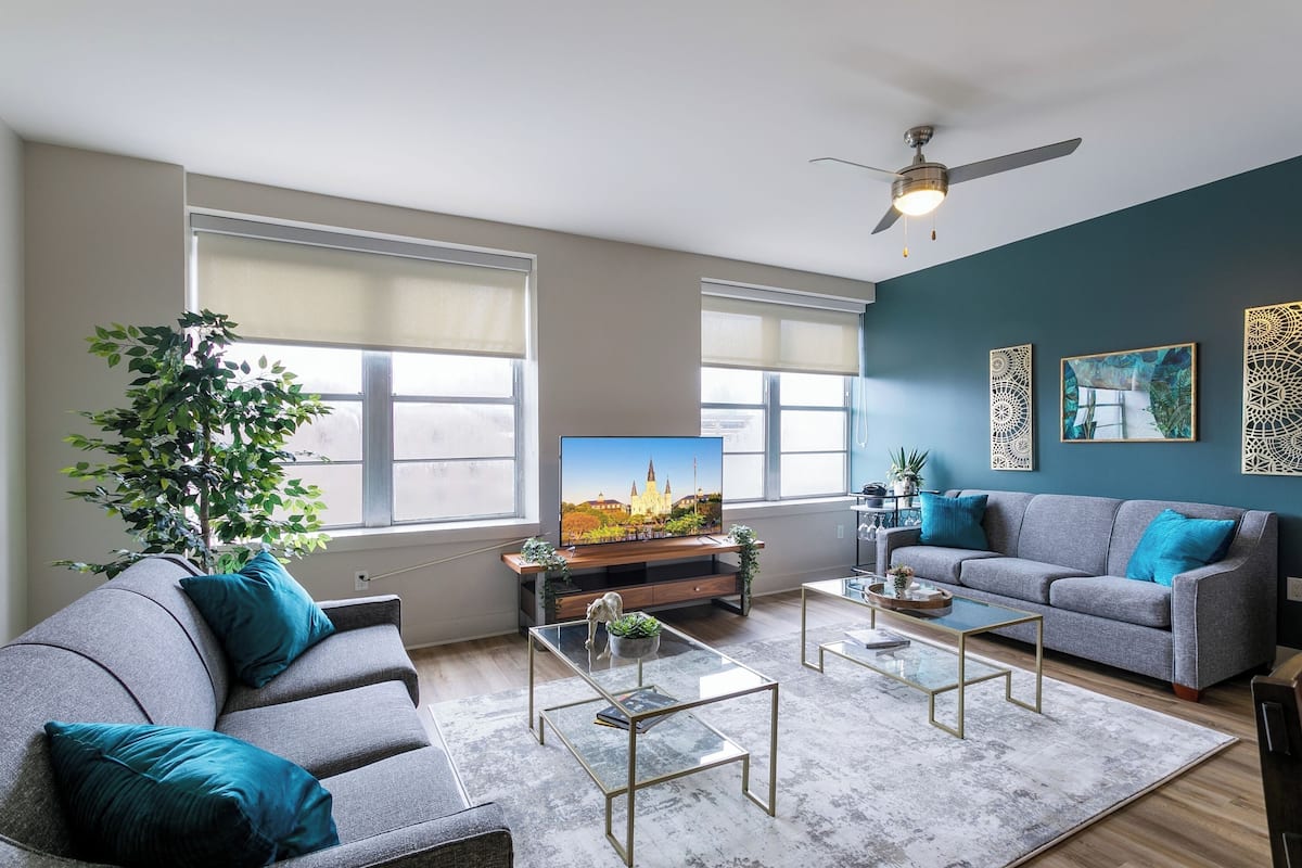 A modern living room with a grey sofa, a glass coffee table, and a television on a wooden stand.
