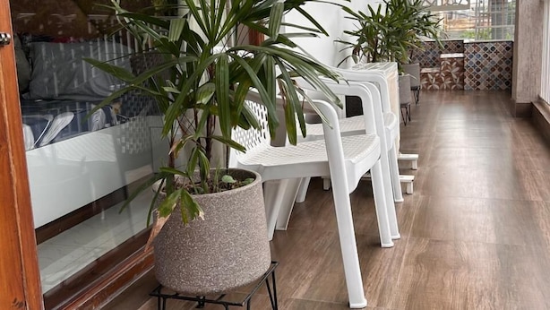 Ein Balkon mit Topfpflanzen, weißen Plastikstühlen und Holzboden.