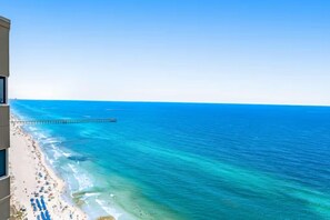 Una spiaggia con acqua cristallina, un molo che si protende verso il mare e un edificio con balconi che si affaccia sulla spiaggia.