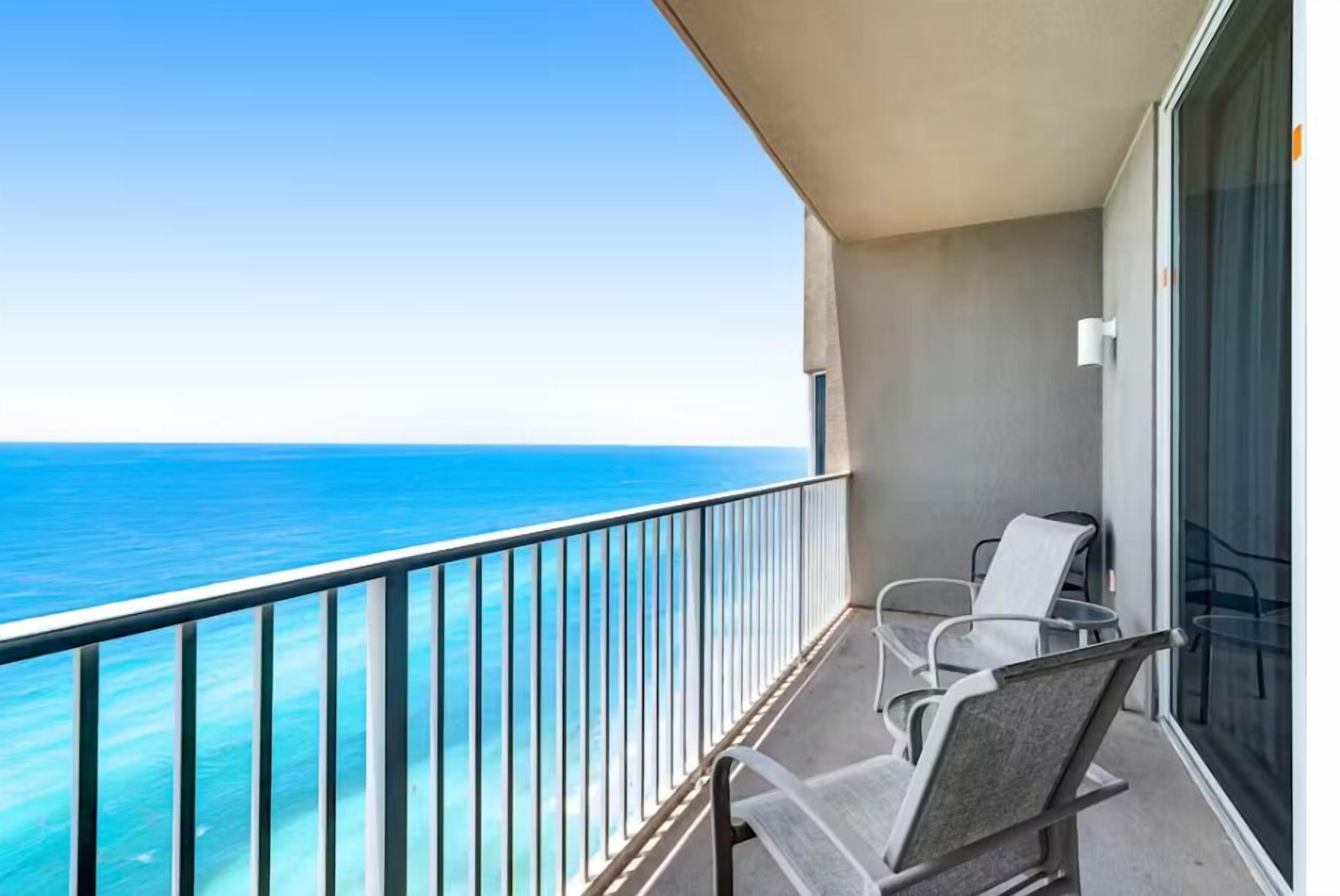 A balcony with a view of the ocean, two chairs, and a glass door.