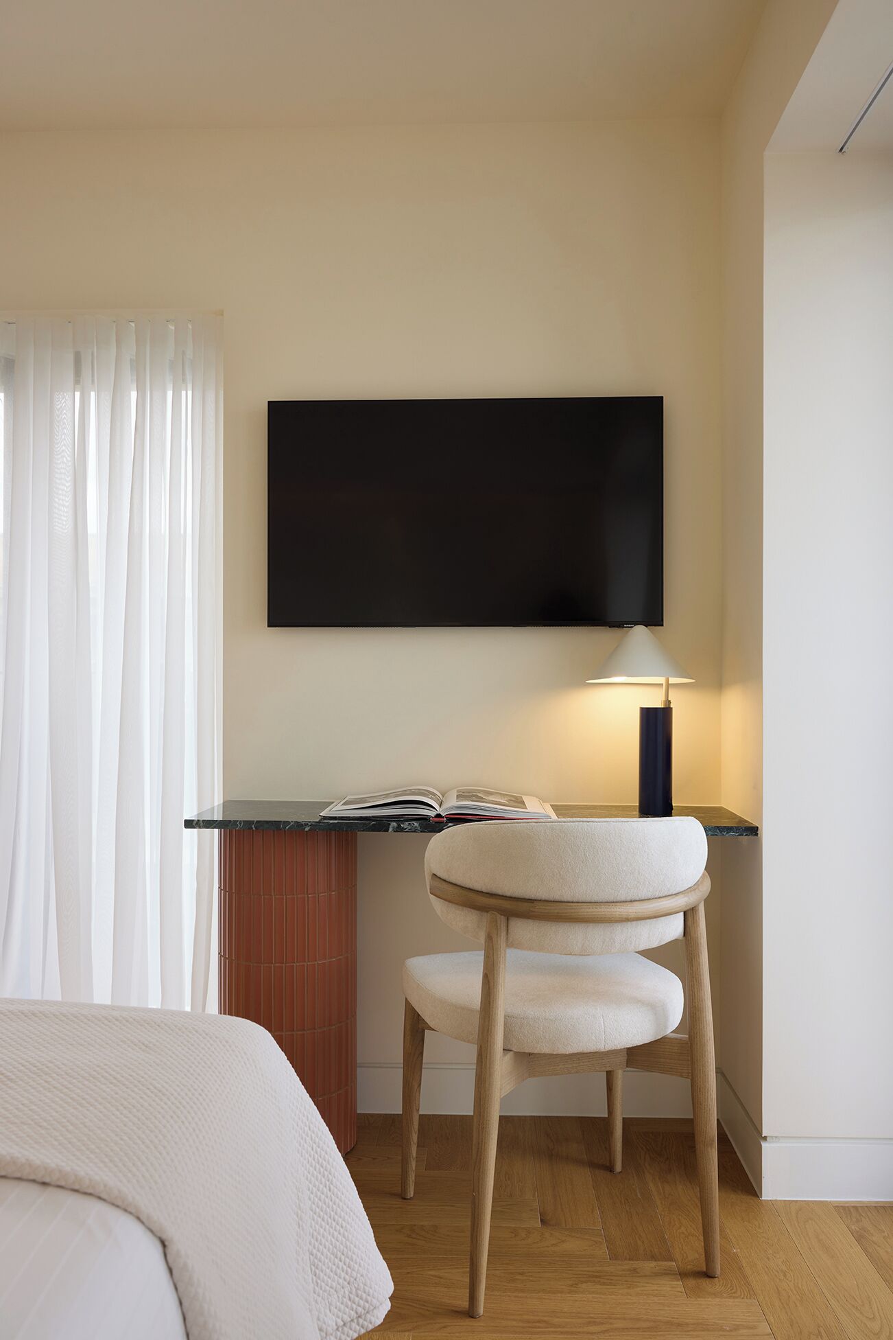 A modern hotel room with a bed, a desk with a flat-screen TV, a lamp, and a chair.