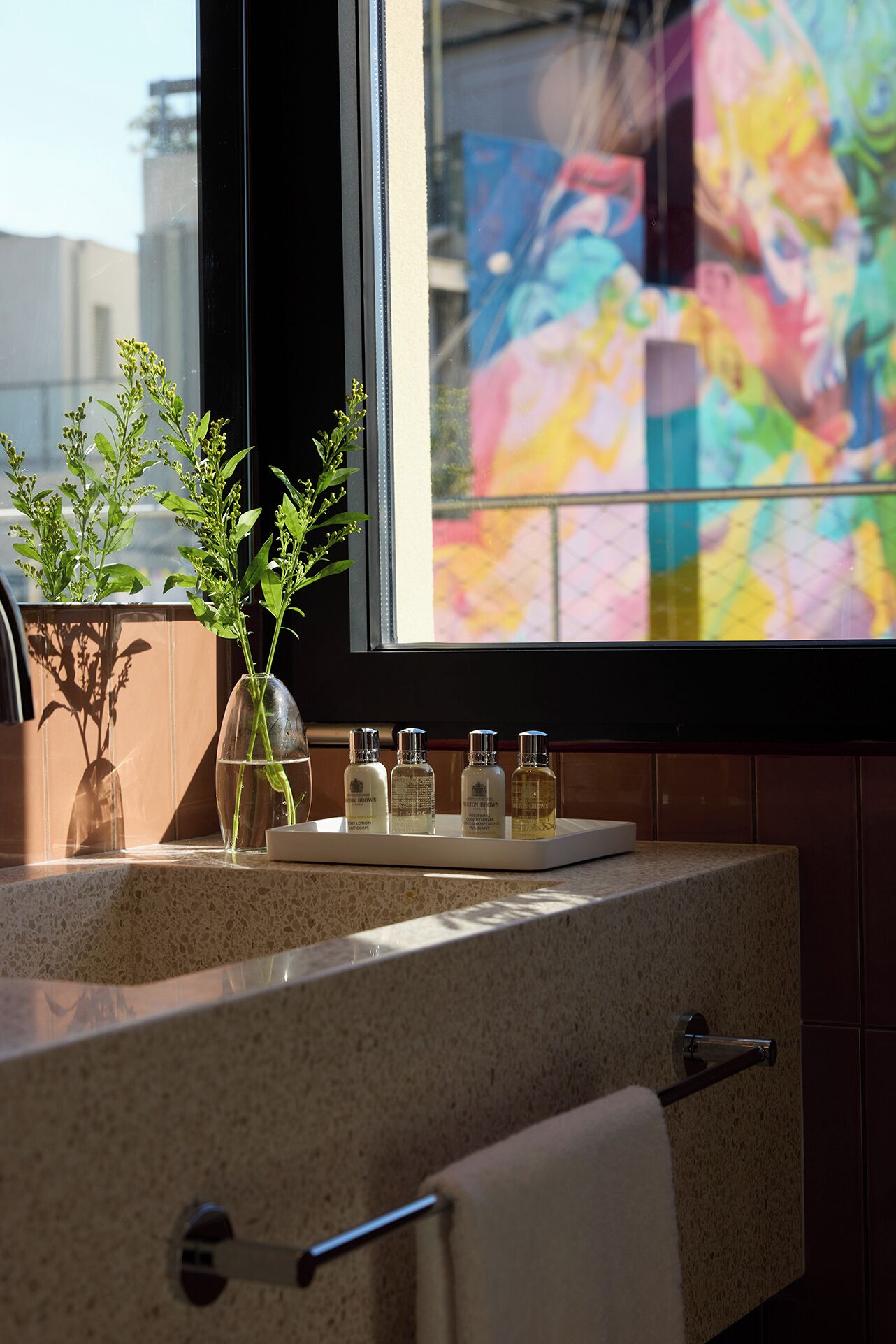 A bathroom vanity with a window, a plant, and toiletries.