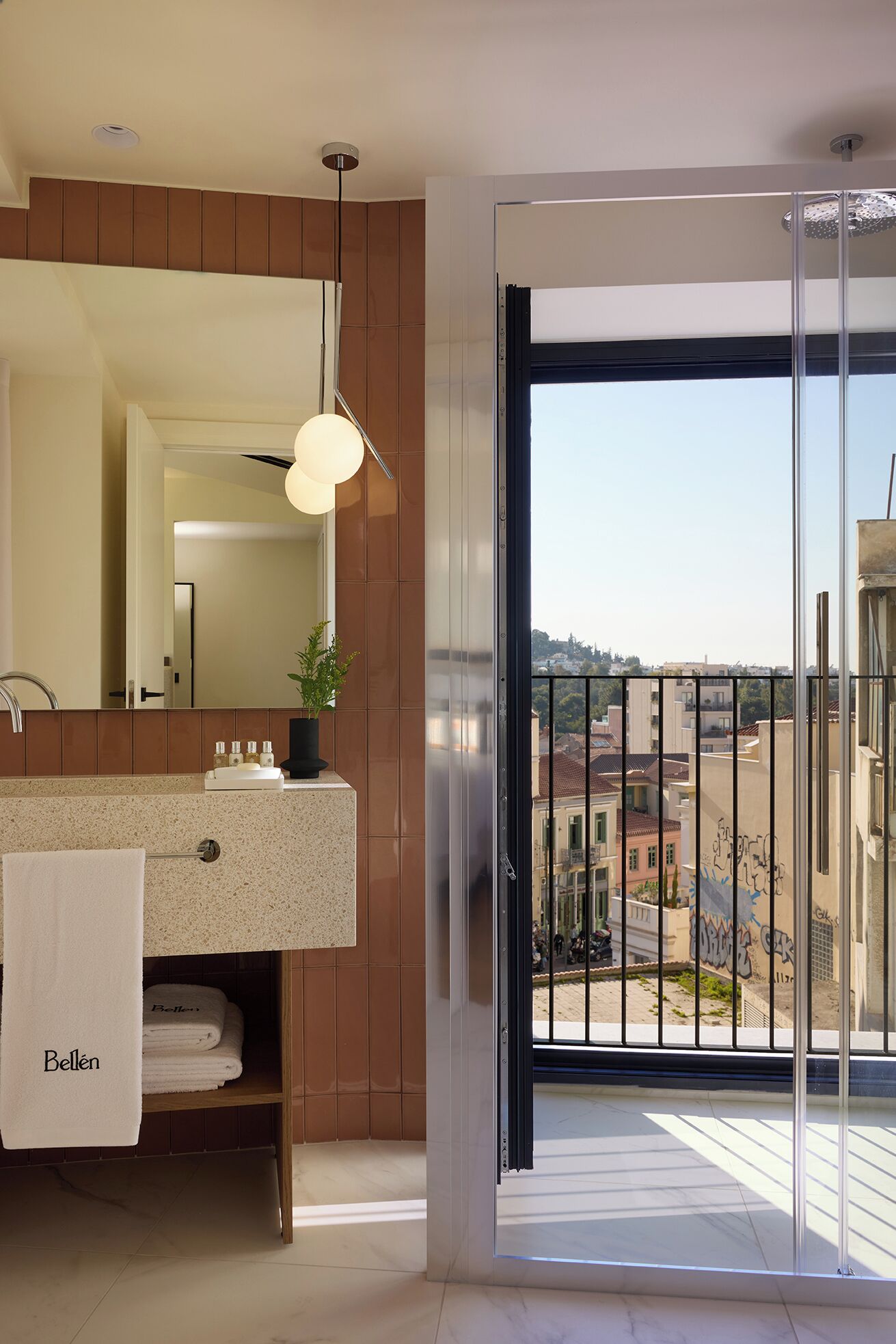 A modern bathroom with a large mirror, a sink with a towel rack, and a view of the city through a sliding door.