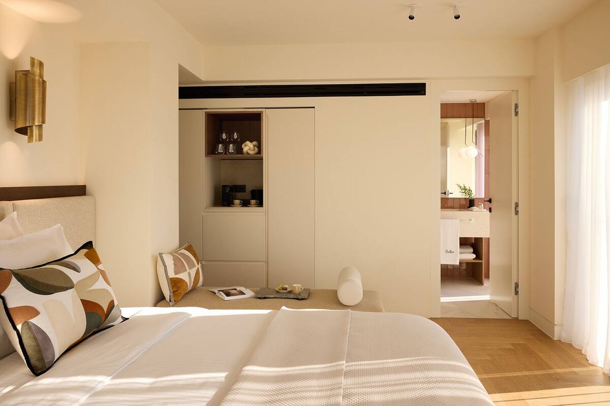 A modern bedroom with a large bed, bedside tables, a built-in shelf with glassware, and a view into a bathroom.