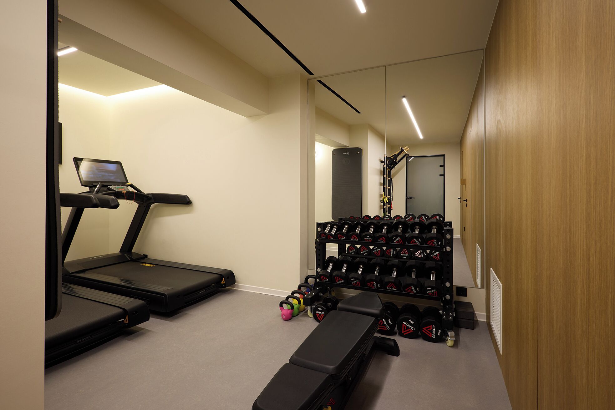 Une salle de sport à domicile équipée d’un tapis de course, d’un banc et d’un porte-haltères.