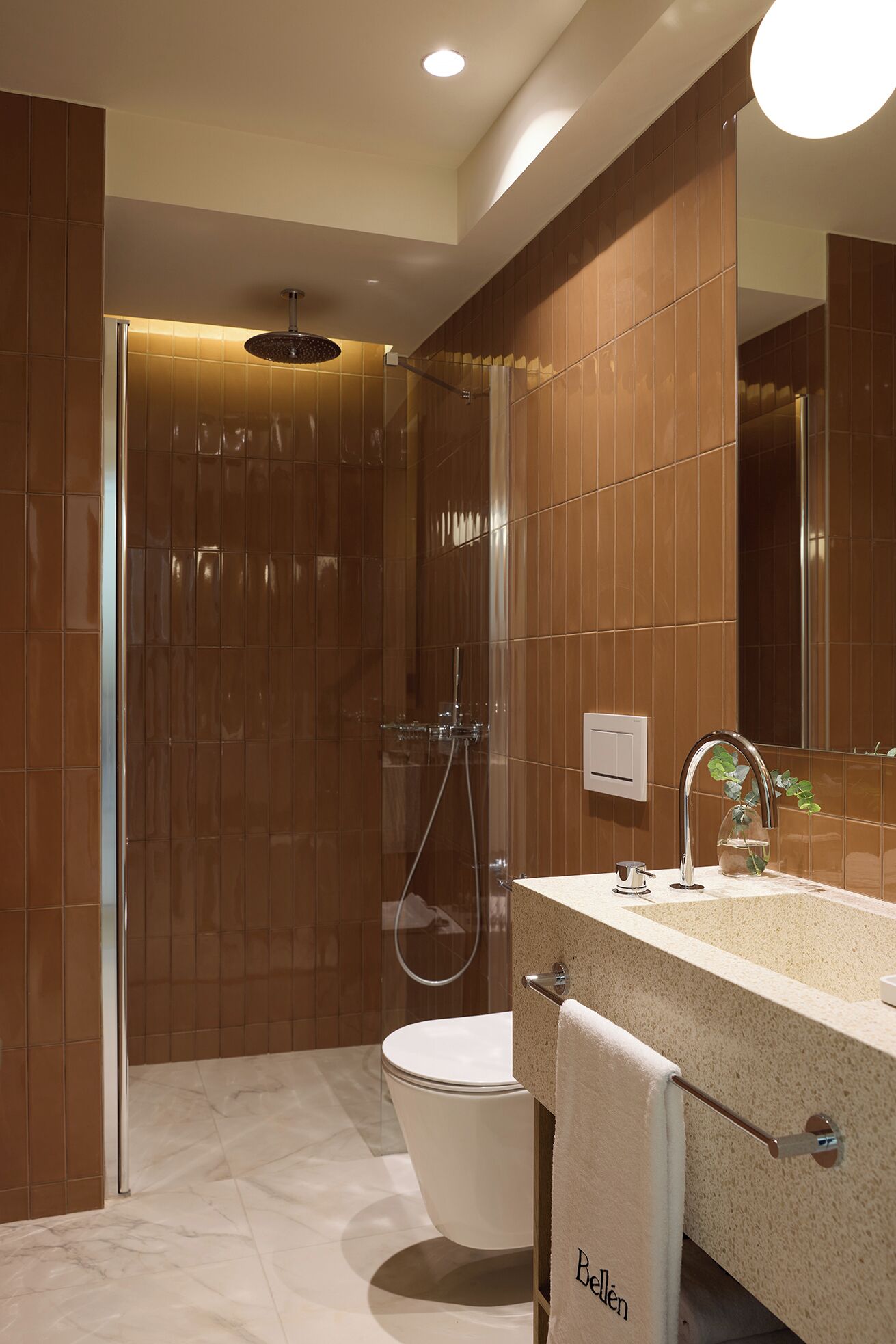 Une salle de bain moderne avec une douche à parois de verre, des toilettes blanches et un lavabo beige doté d’un porte-serviettes.