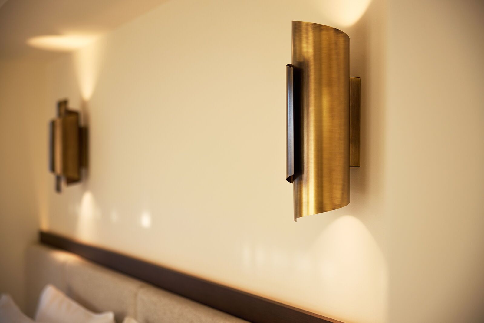 A modern hotel room with a sleek, metallic wall-mounted light fixture and a clean, minimalist design.