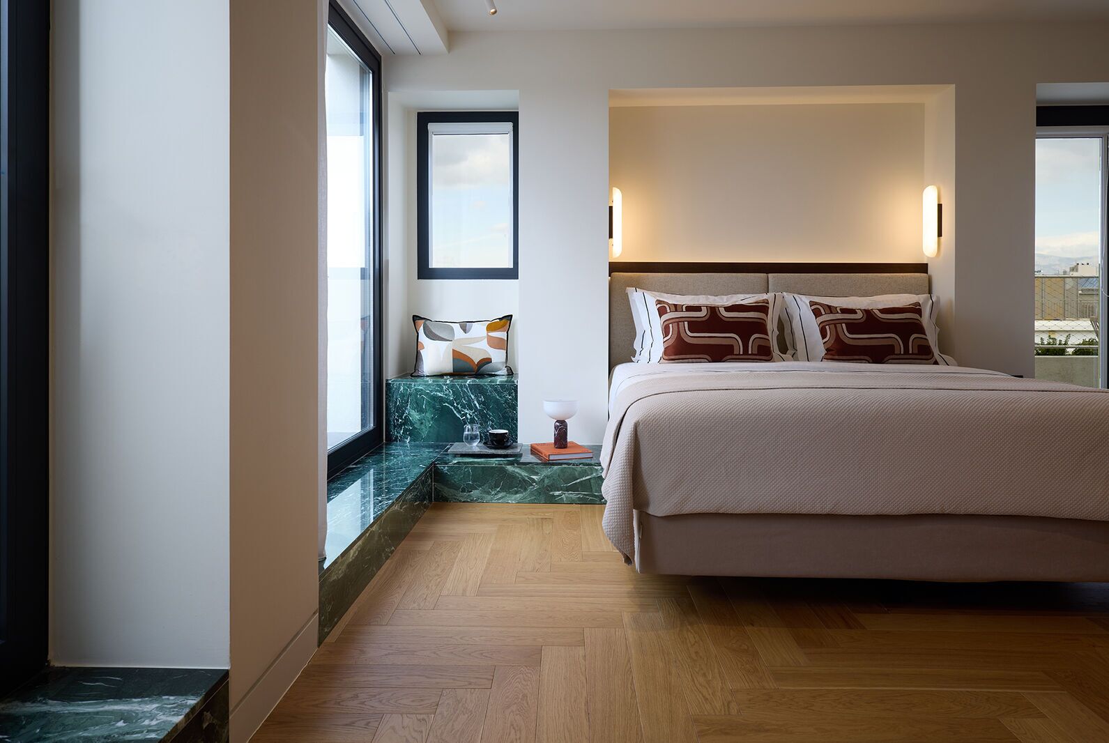 A hotel room with a bed, a nightstand, a marble bench, and a large window.